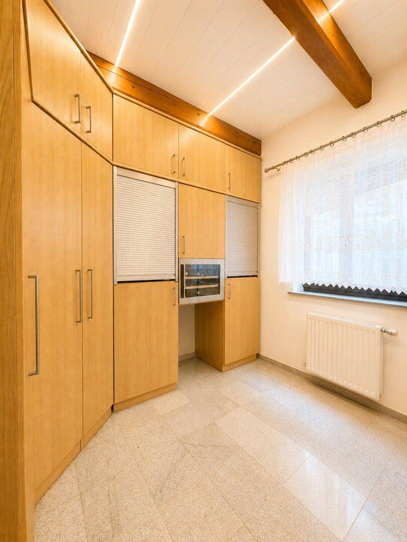 Raum mit maßgefertigten Holzschränken, kleinem Schreibtischbereich und sichtbarem Deckenbalken.