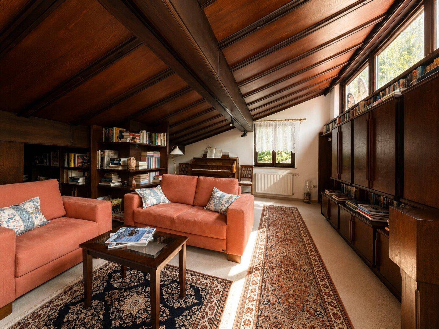 Gemütliches Wohnzimmer mit Holzbalkendecke, Bücherregalen und bequemen Sofas.