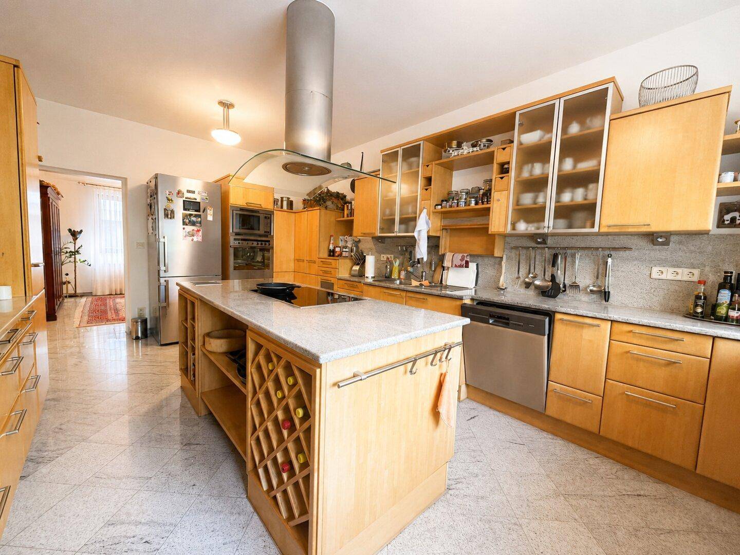 Küche mit Holzschränken, Kücheninsel, Kühlschrank, Geschirrspüler und integriertem Weinregal.