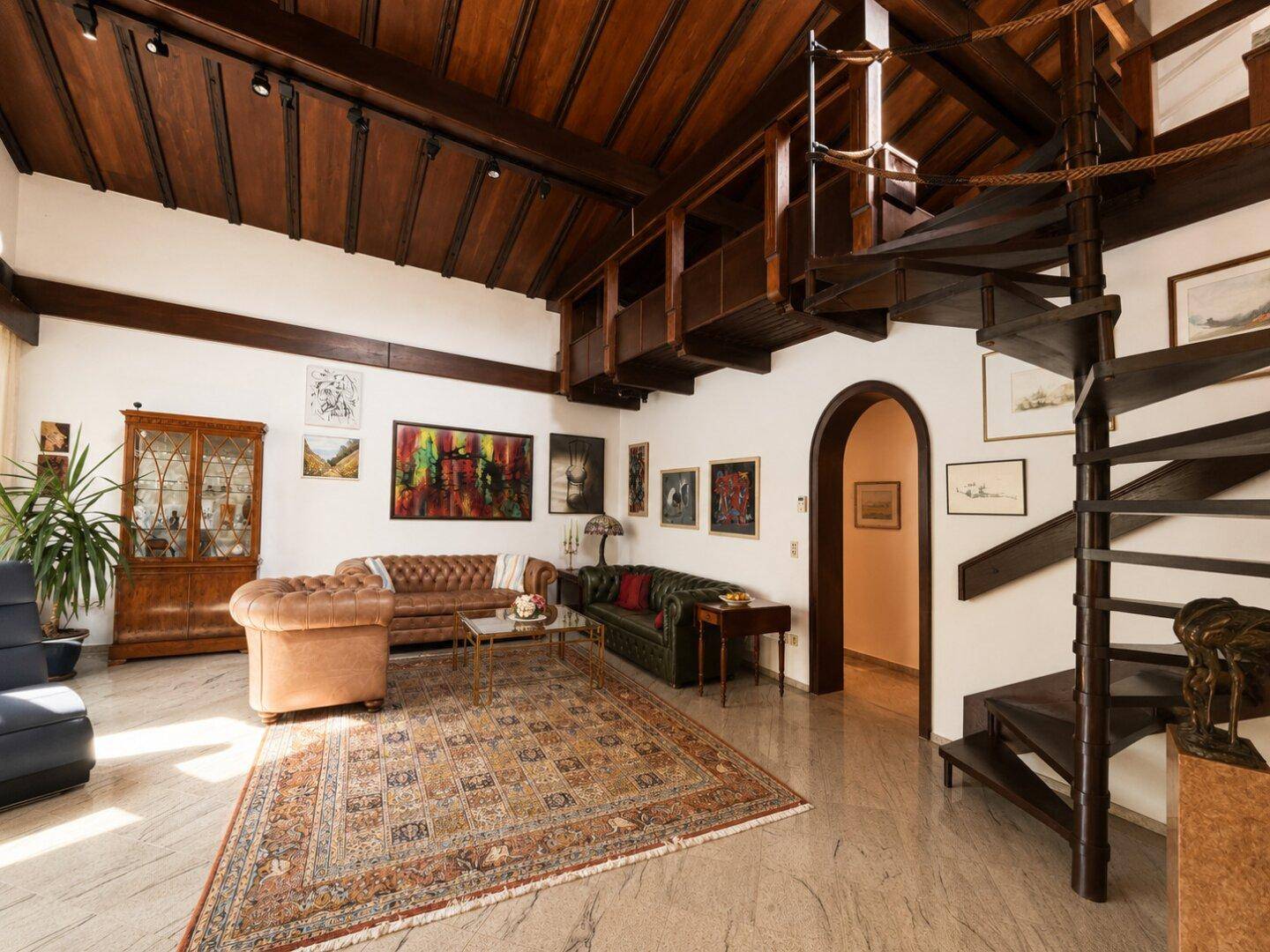 Geräumiges Wohnzimmer mit Holzbalkendecke, Wendeltreppe und vielfältiger Kunstdekoration.