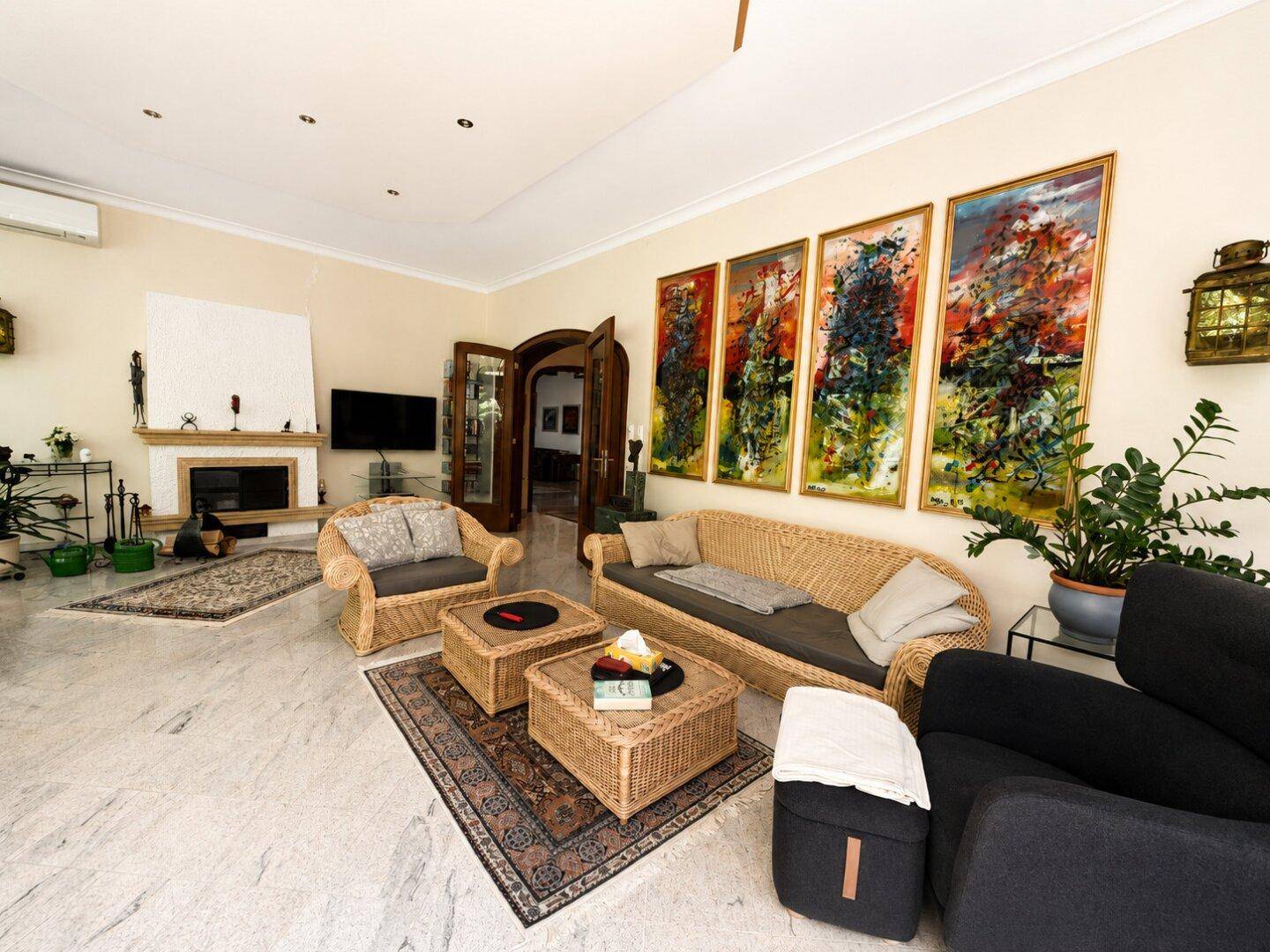 Helles Wohnzimmer mit Rattanmöbeln, Kamin und farbenfrohen Kunstwerken an der Wand.
