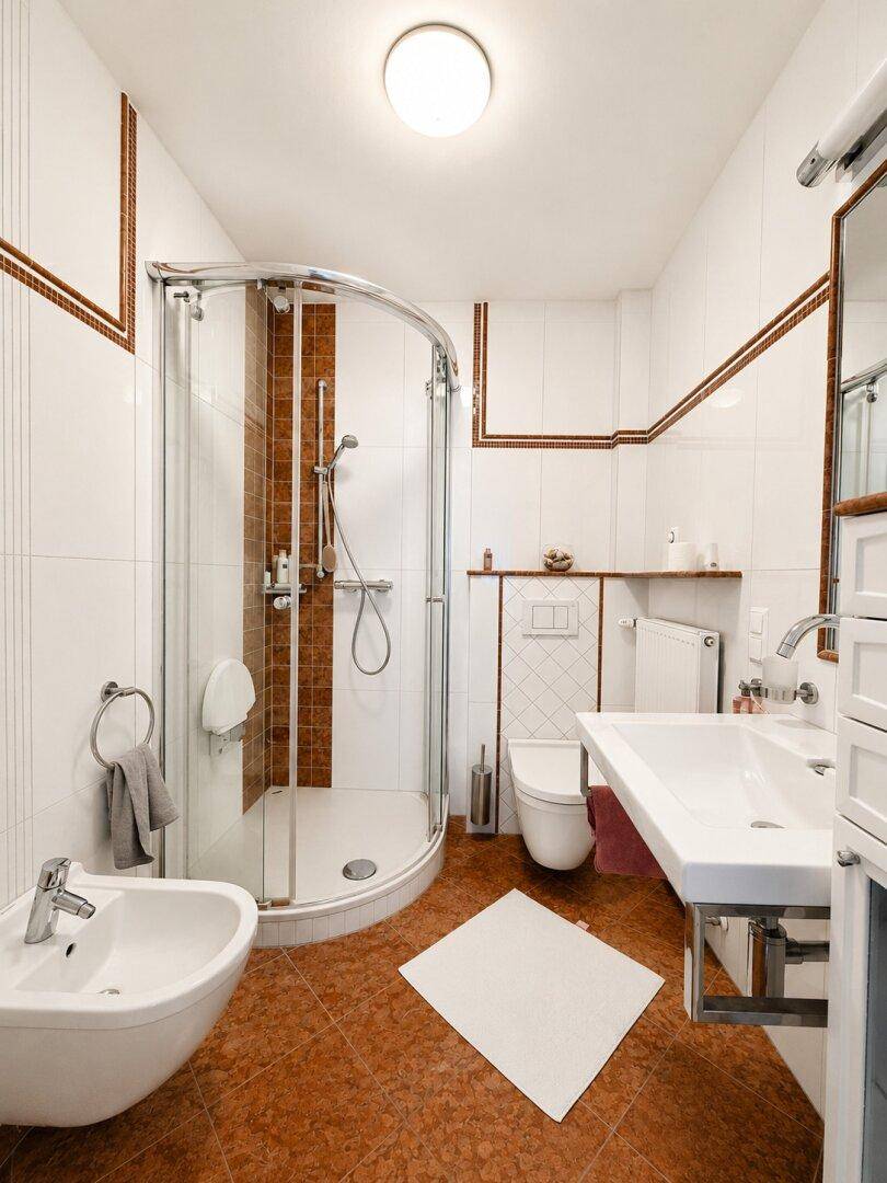Modernes Badezimmer mit Duschkabine, Bidet und weißen Fliesen mit braunen Akzenten.