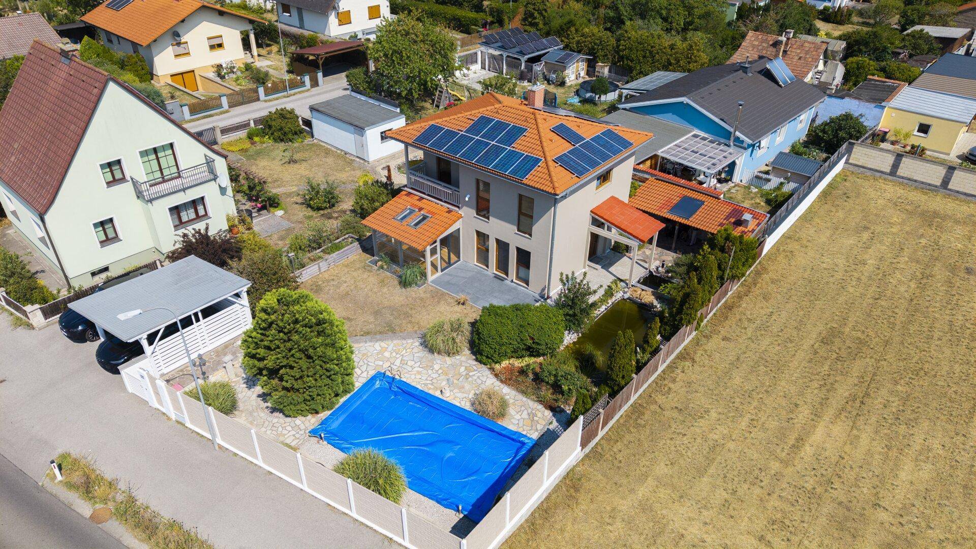 Vogelperspektive des Einfamilienhauses mit Solaranlage, Pool und angrenzendem Feld.