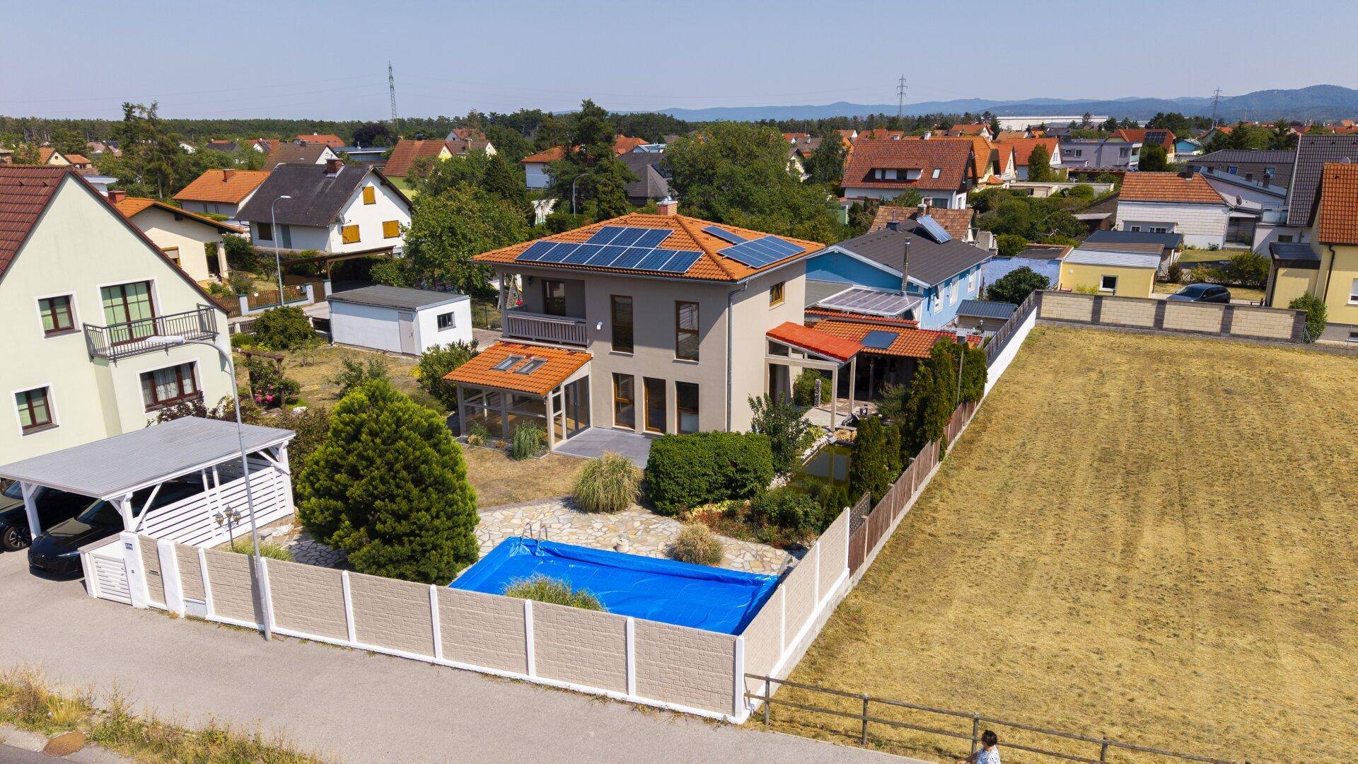 Panoramablick auf das Haus mit Solaranlage, Pool und angrenzendem Feld, in sonniger Lage.