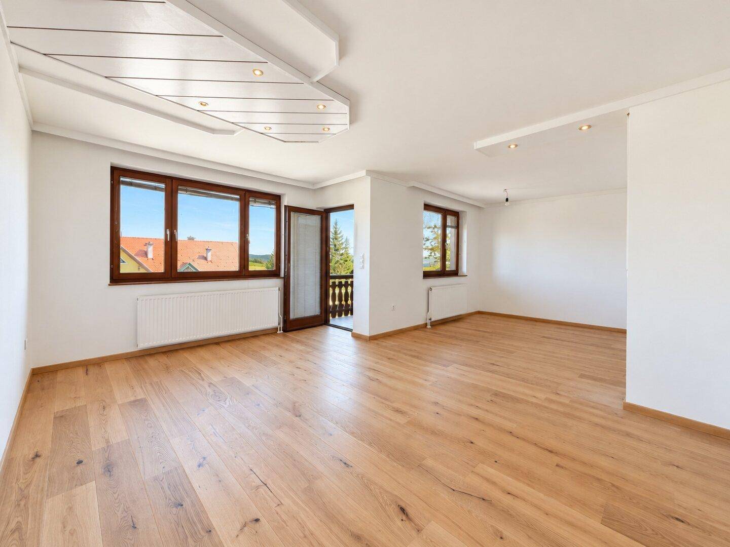 Geräumiges Wohnzimmer mit Holzboden, großen Fenstern und Zugang zu einem Balkon.