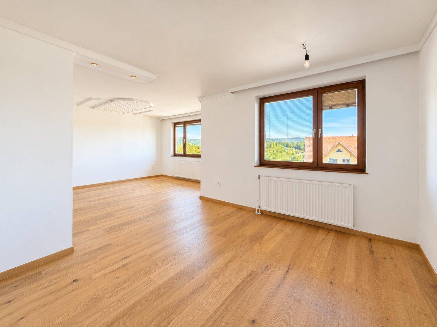 Helles Wohnzimmer mit Holzboden und weitem Blick durch die großen Fenster in die Landschaft.