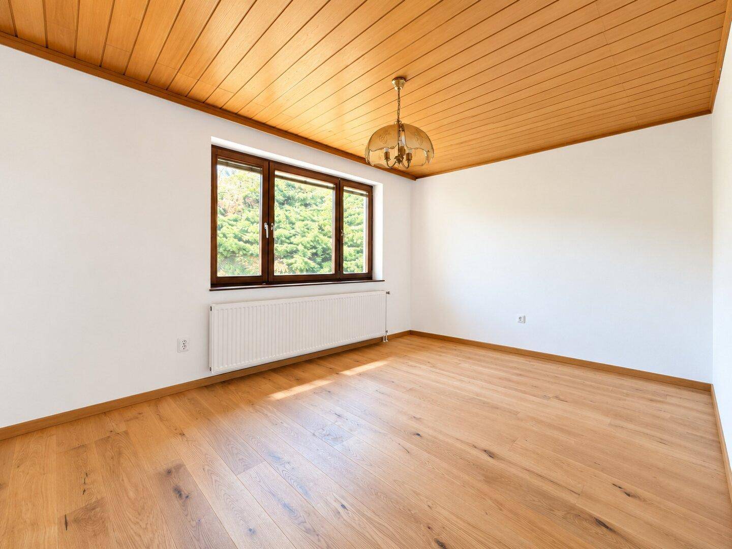 Schlafzimmer mit Holzboden, Holzdecke und großem Fenster, das viel Tageslicht hereinlässt.