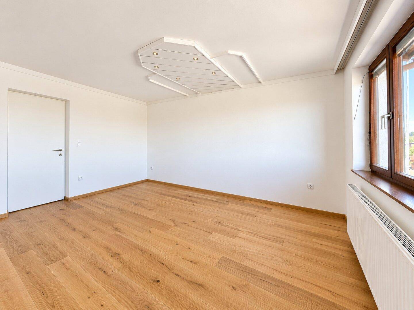 Helles Schlafzimmer mit Holzboden und moderner Deckenbeleuchtung, bereit zur individuellen Einrichtung.
