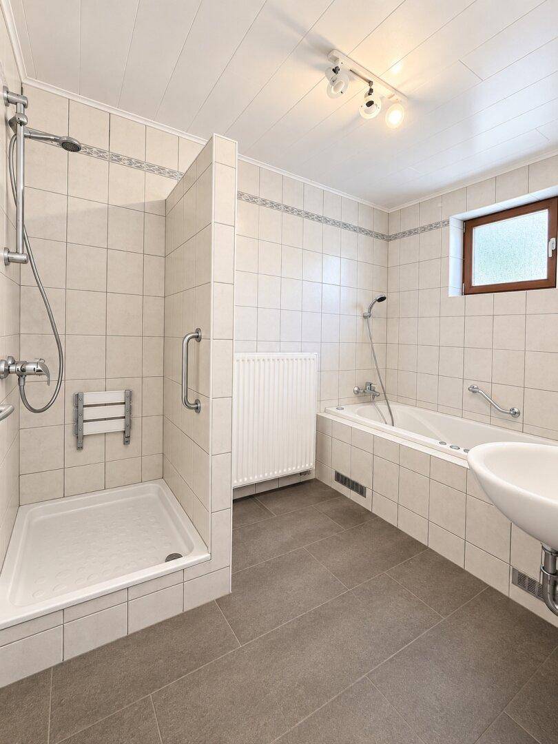 Badezimmer mit Dusche, Badewanne und Fenster, ausgestattet mit Haltegriffen für Komfort.