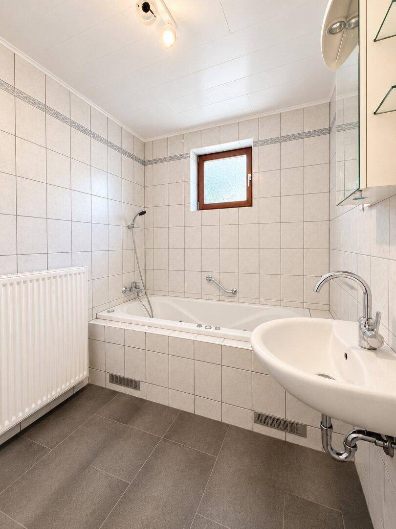 Helles Badezimmer mit Badewanne, Waschbecken und Fenster, in gutem und gepflegtem Zustand.