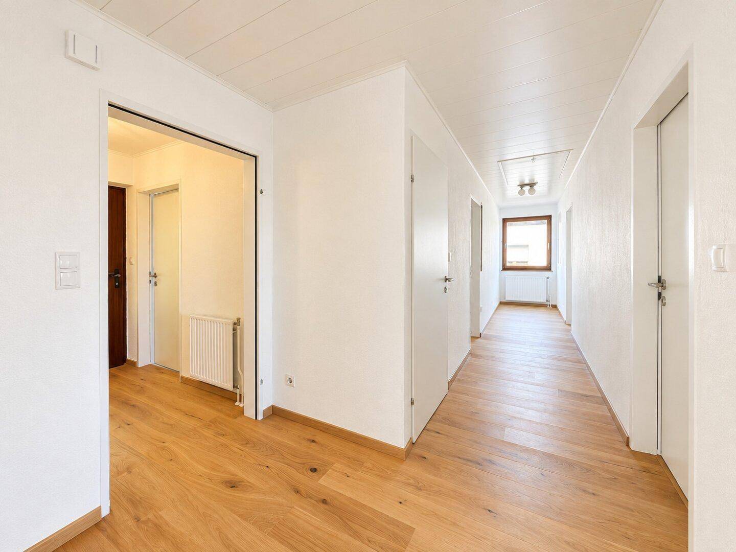 Langer, heller Flur mit Holzboden und mehreren Türen, der verschiedene Räume verbindet.