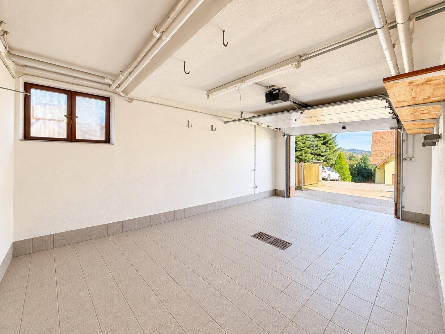 Geräumige Garage mit Fliesenboden und automatischem Tor, bietet Platz für ein Fahrzeug.