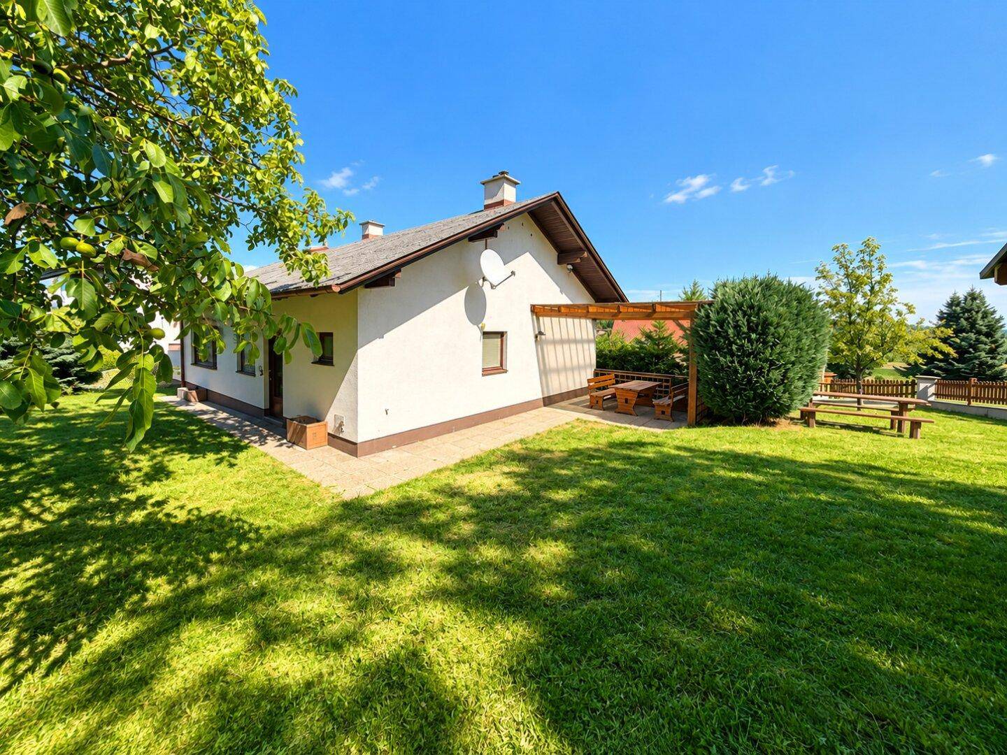 Hausfassade mit überdachter Terrasse und großem, gepflegtem Gartenbereich unter blauem Himmel.