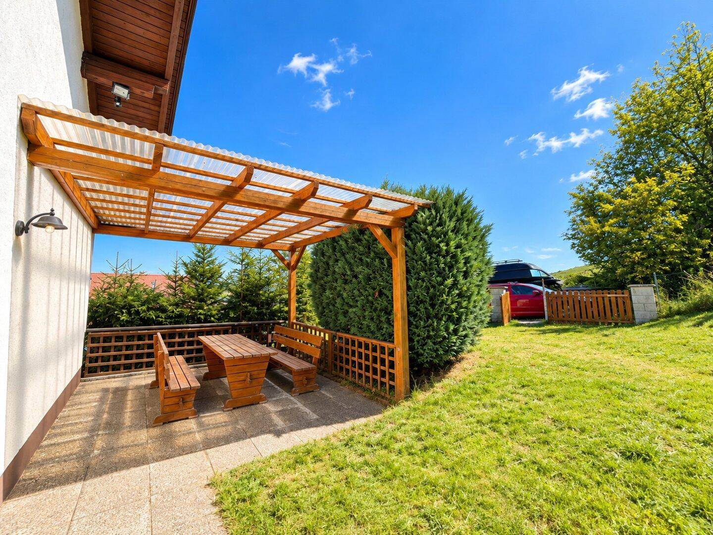 Überdachte Terrasse mit rustikalen Holzmöbeln, umgeben von Grün und mit Blick in den Garten.