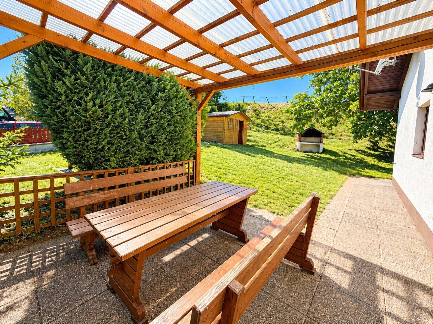 Gemütliche überdachte Terrasse mit Holztisch und Bänken, ideal für Mahlzeiten im Freien mit Gartenblick.