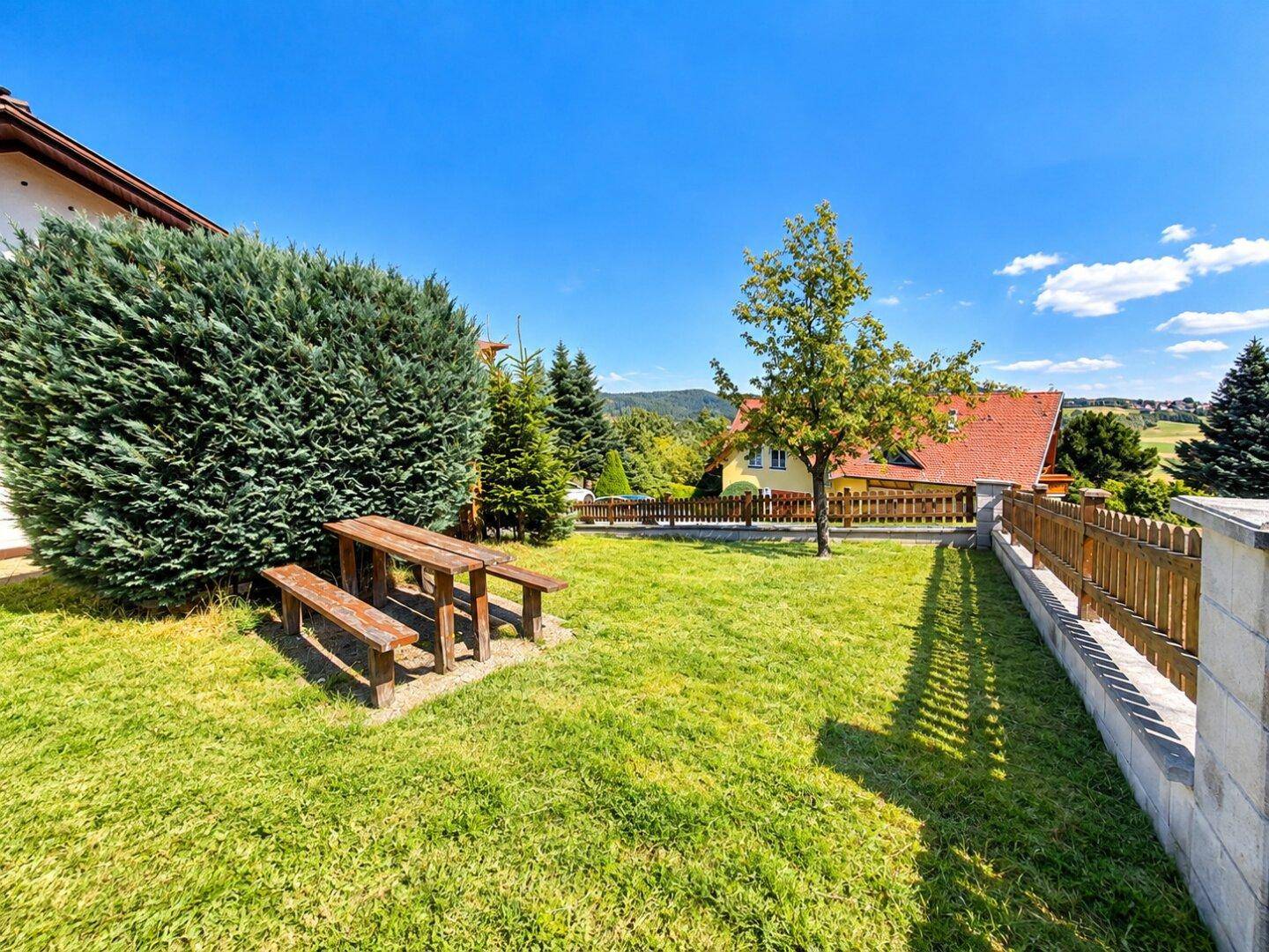 Gepflegter Garten mit Rasenfläche und einem Picknicktisch, umgeben von Bäumen und Sträuchern.