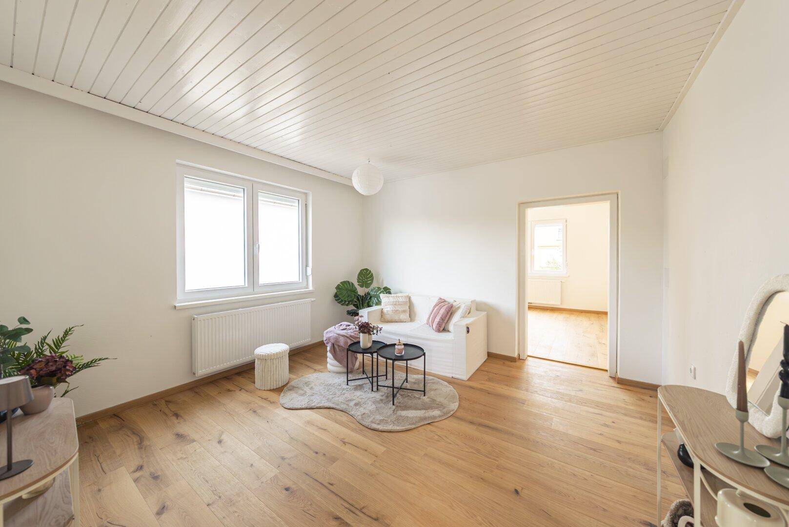 Gemütliches Wohnzimmer mit hellem Holzboden, weißer Deckenverkleidung und moderner Dekoration.