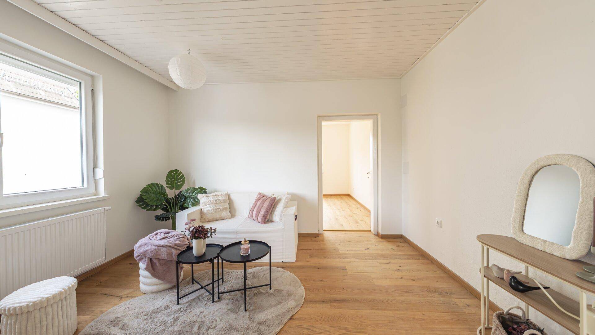 Helles Wohnzimmer mit Holzboden, weißer Deckenverkleidung und minimalistischer Einrichtung.