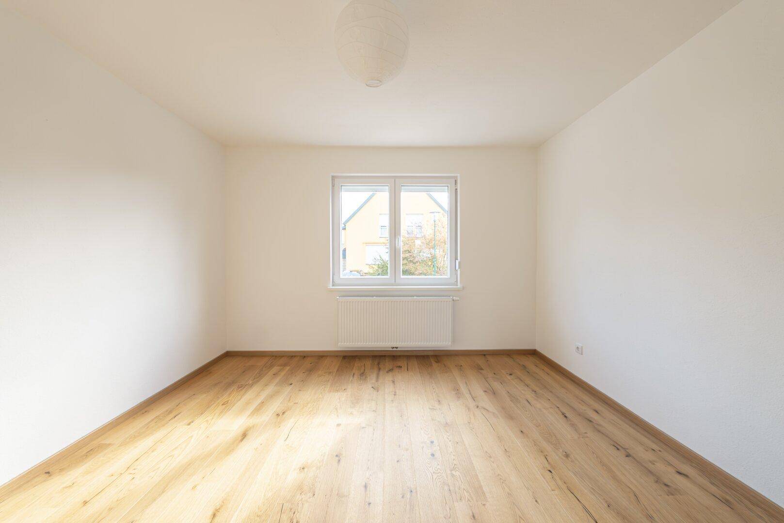 Helles, leeres Zimmer mit Holzboden und weiß gestrichenen Wänden, bereit zur individuellen Gestaltung.