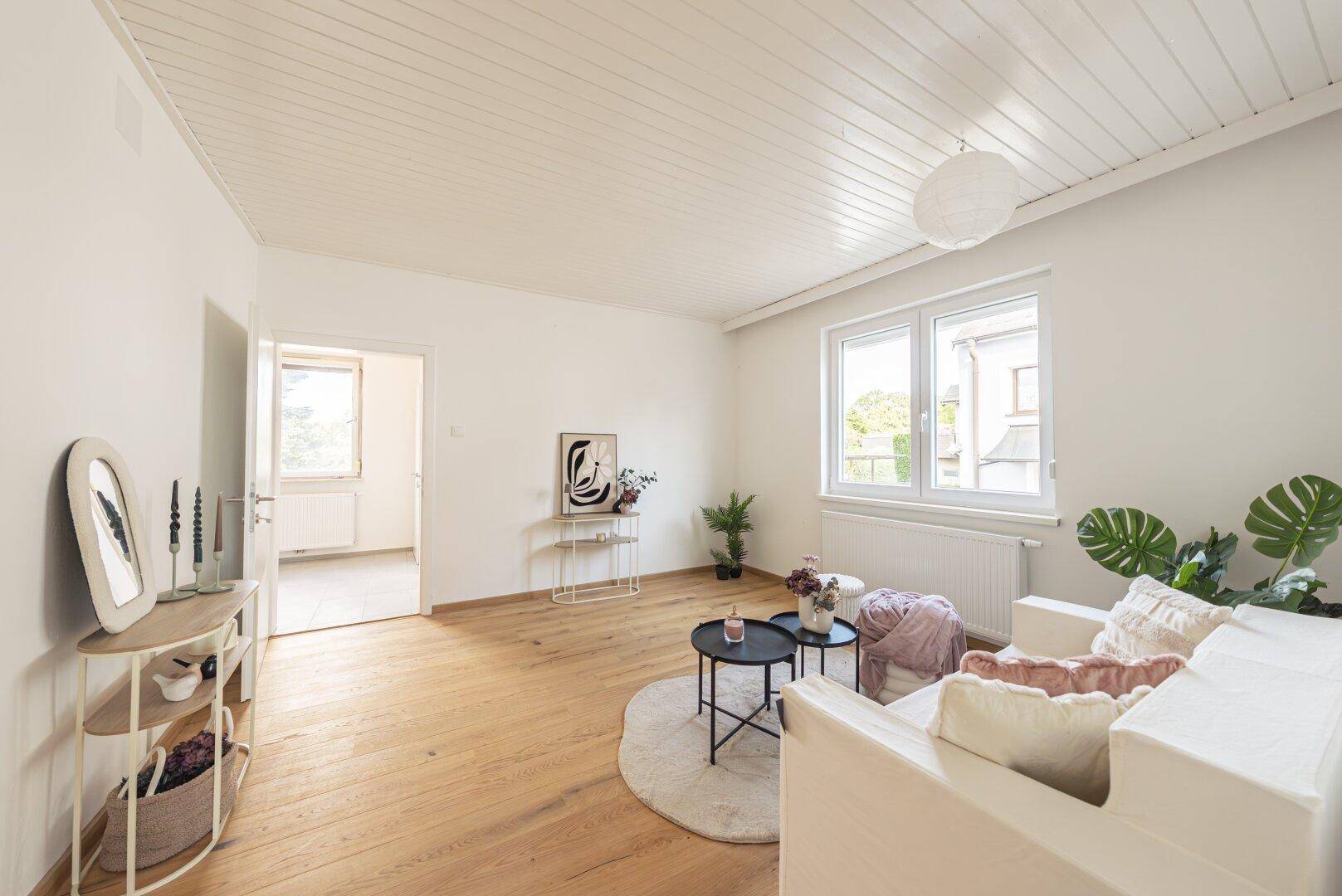 Modern eingerichtetes Wohnzimmer mit Holzboden, weißer Deckenverkleidung und viel Tageslicht.