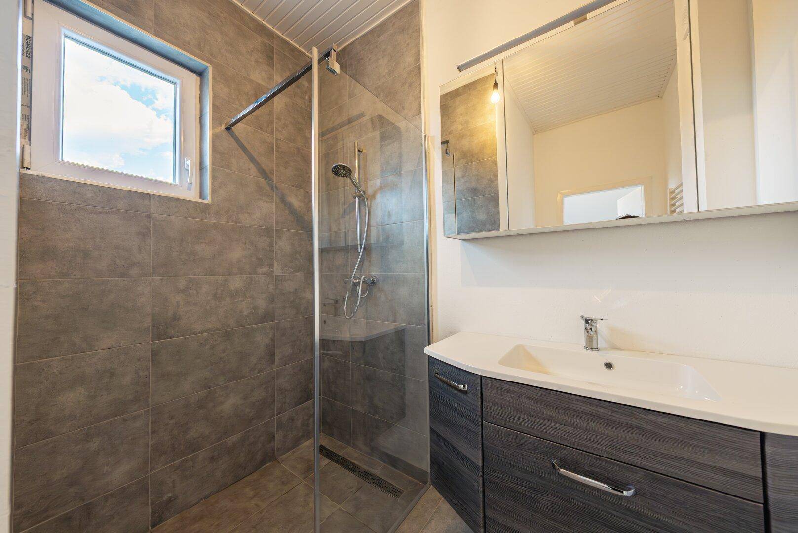 Modernes Badezimmer mit grauen Fliesen, ebenerdiger Dusche und Einzelwaschbecken.