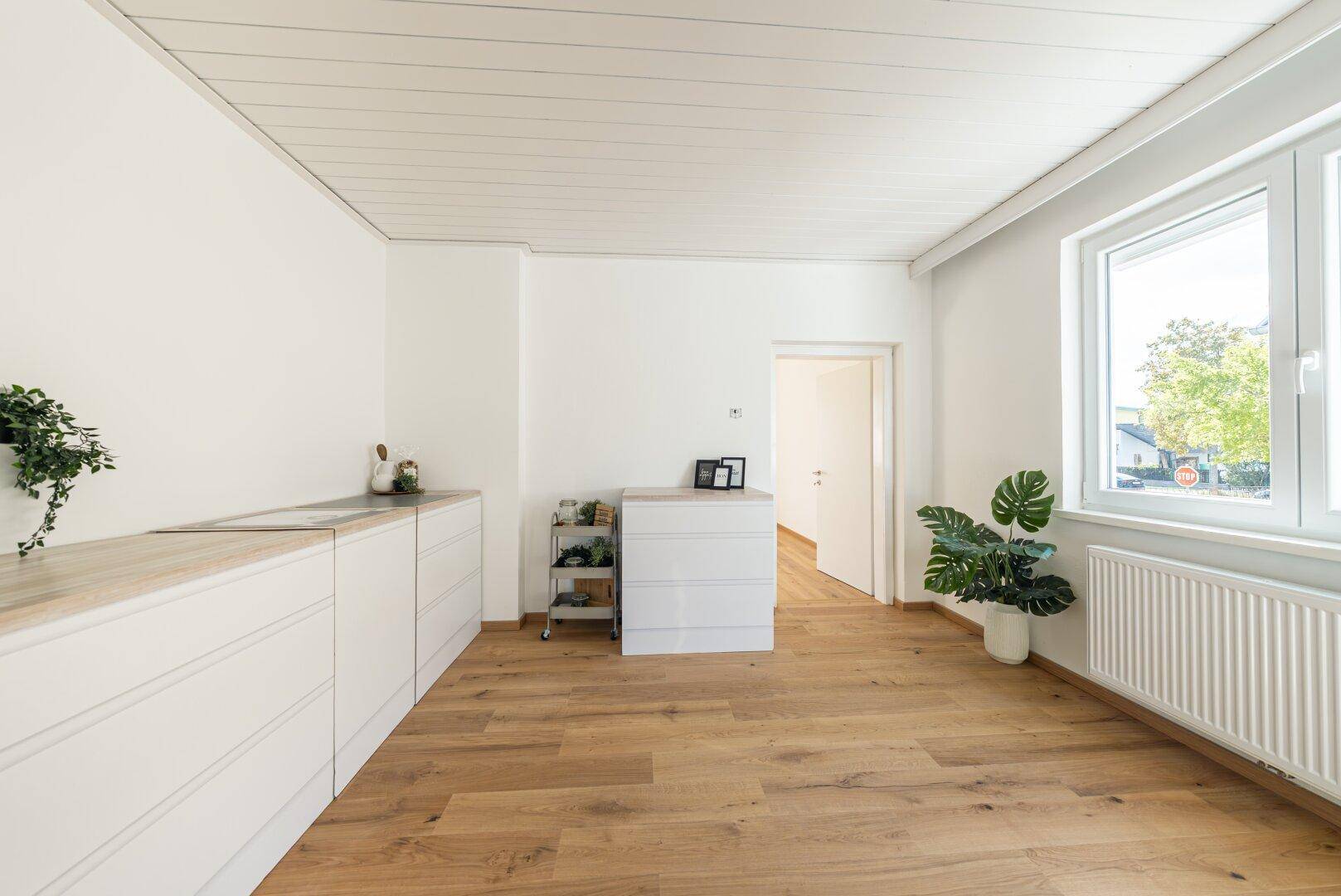 Geräumige Küche mit Holzboden, weißen Unterschränken und viel Tageslicht.
