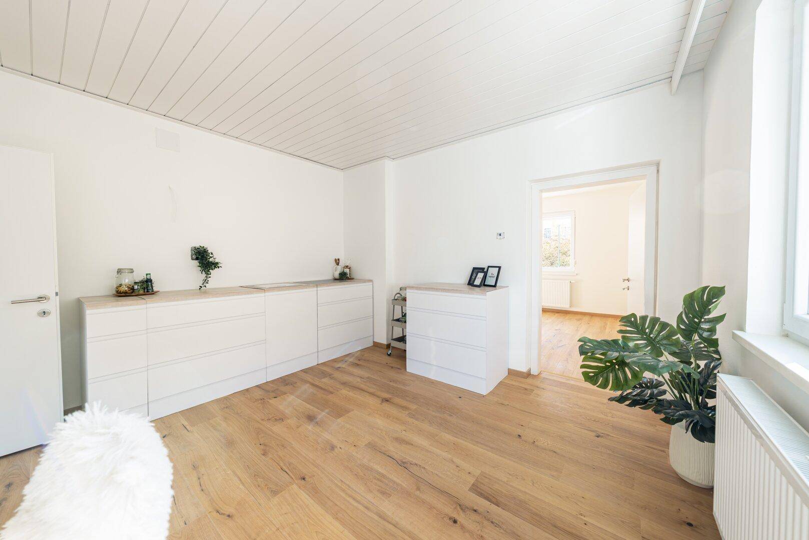 Helle Küche mit Holzboden, weißen Schränken und Blick in den angrenzenden Wohnbereich.