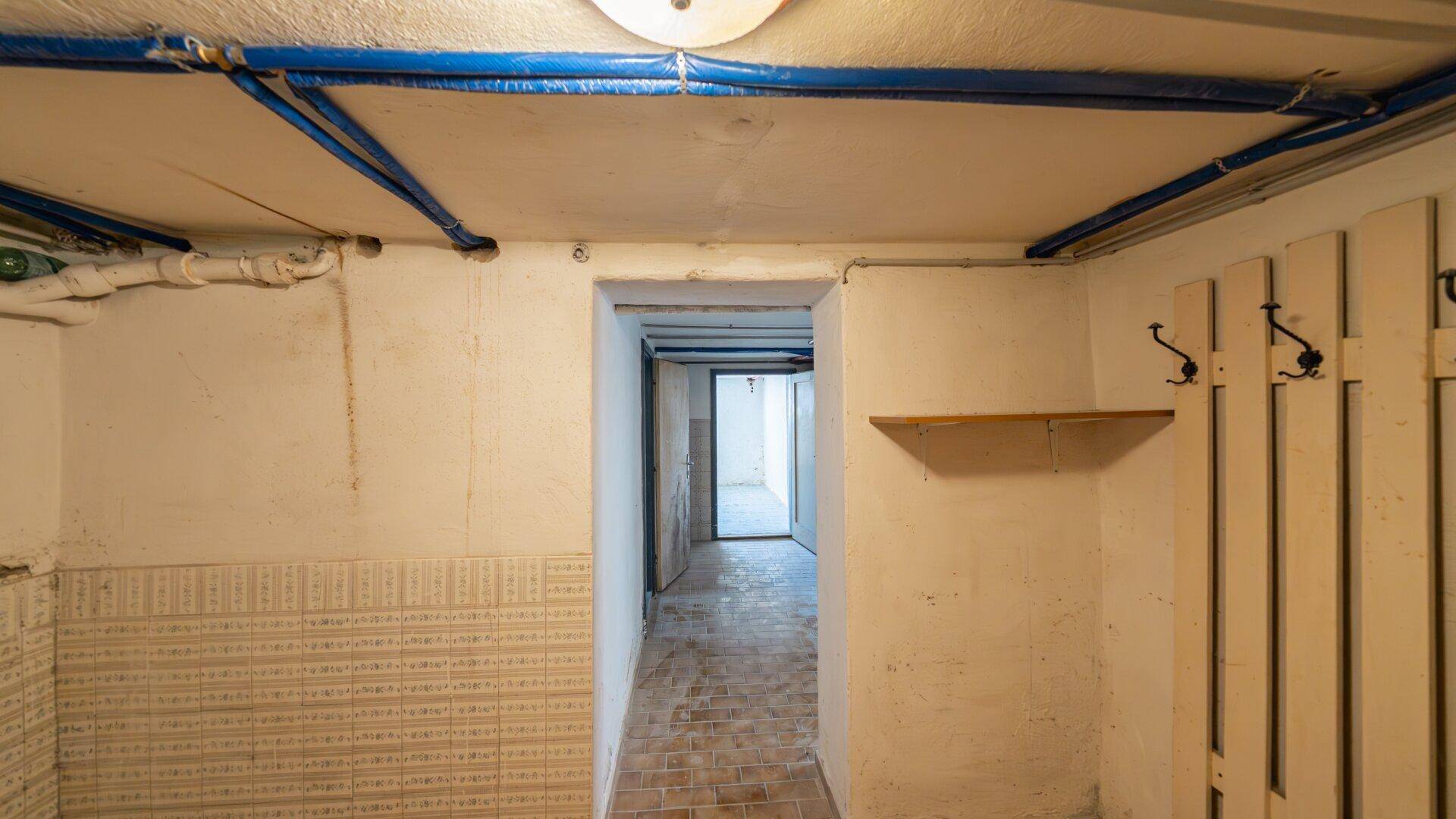 Langer Kellerflur mit sichtbaren Rohren und einfacher Wandverkleidung, führt zu weiteren Kellerräumen.