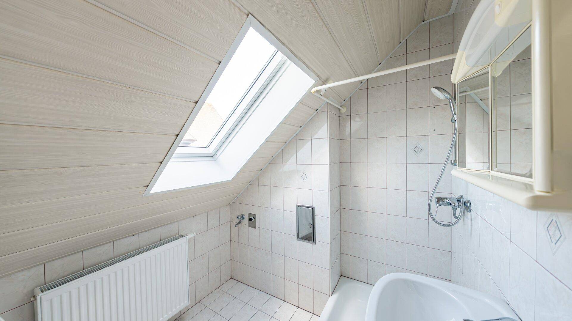 Badezimmer im Dachgeschoss mit Schrägdach, Dachfenster und weißen Fliesen.