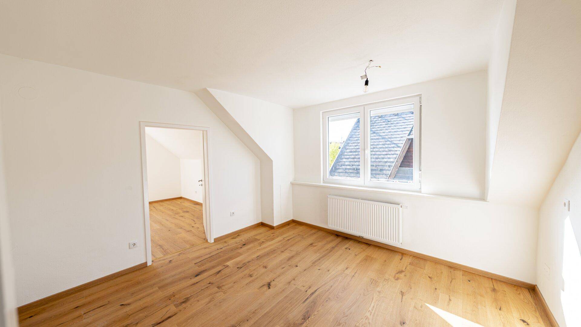 Geräumiges Zimmer im Dachgeschoss mit Holzboden, Schrägdach und Fenster.