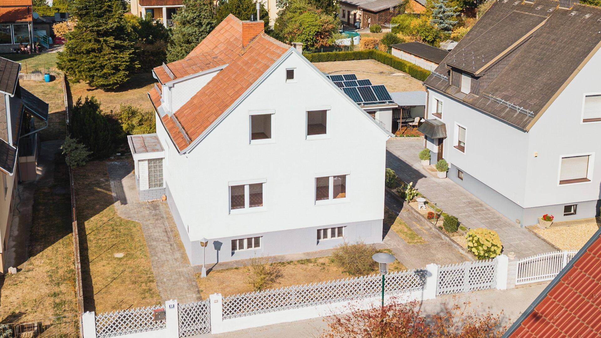 Luftaufnahme des Hauses mit Vorgarten und einem kleinen Anbau, umgeben von weiteren Wohnhäusern.