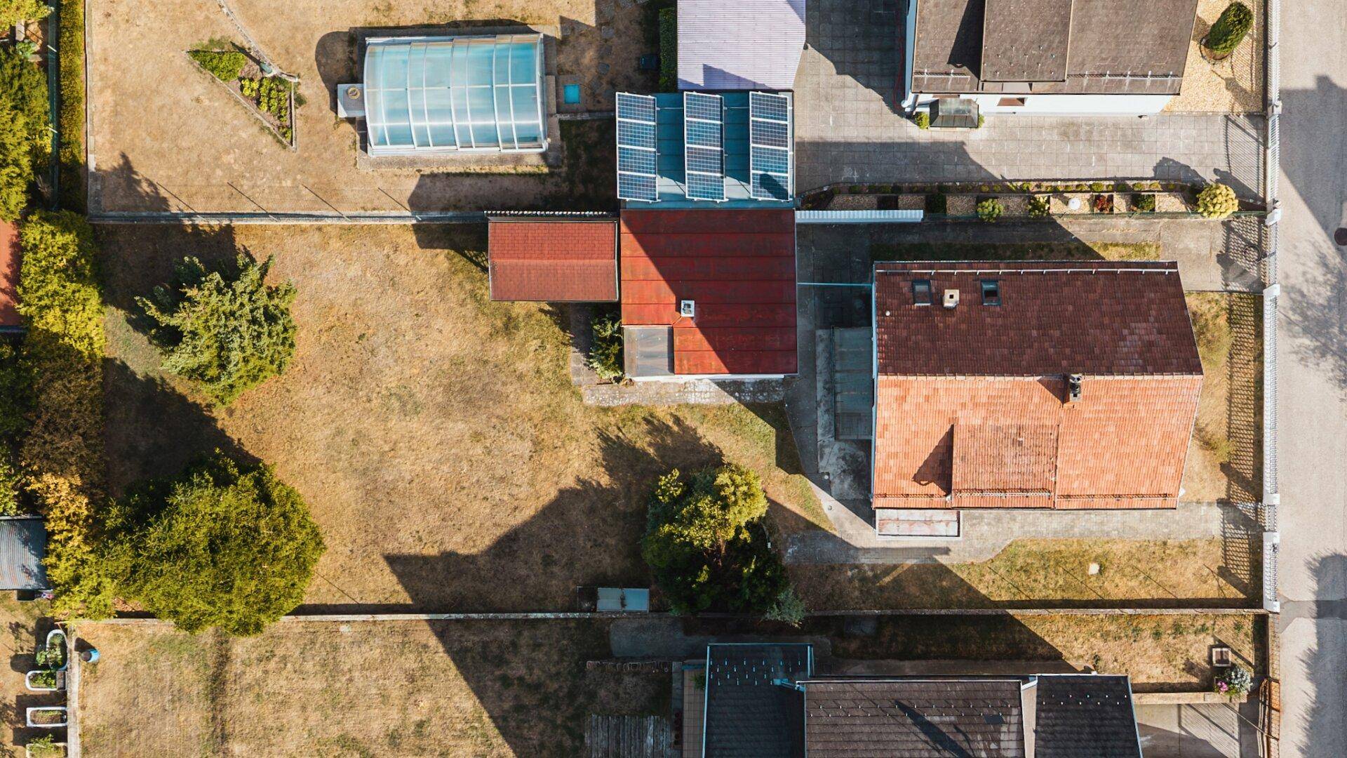 Draufsicht des Grundstücks mit Haus, Garage, Photovoltaikanlage und großem, trockenem Rasenbereich.