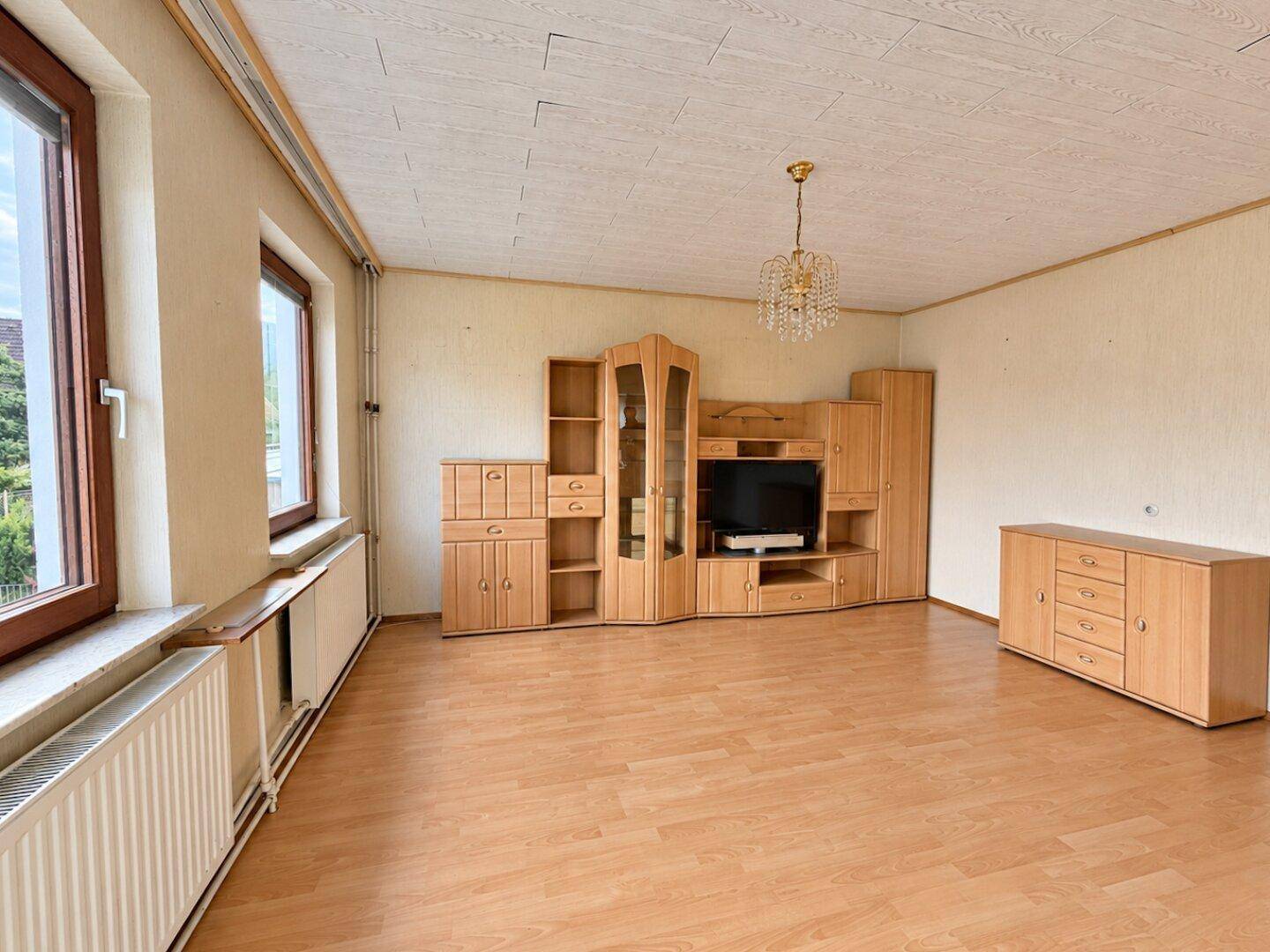 Geräumiges Wohnzimmer mit Laminatboden, Holzmöbeln und einem Kronleuchter an der Decke.
