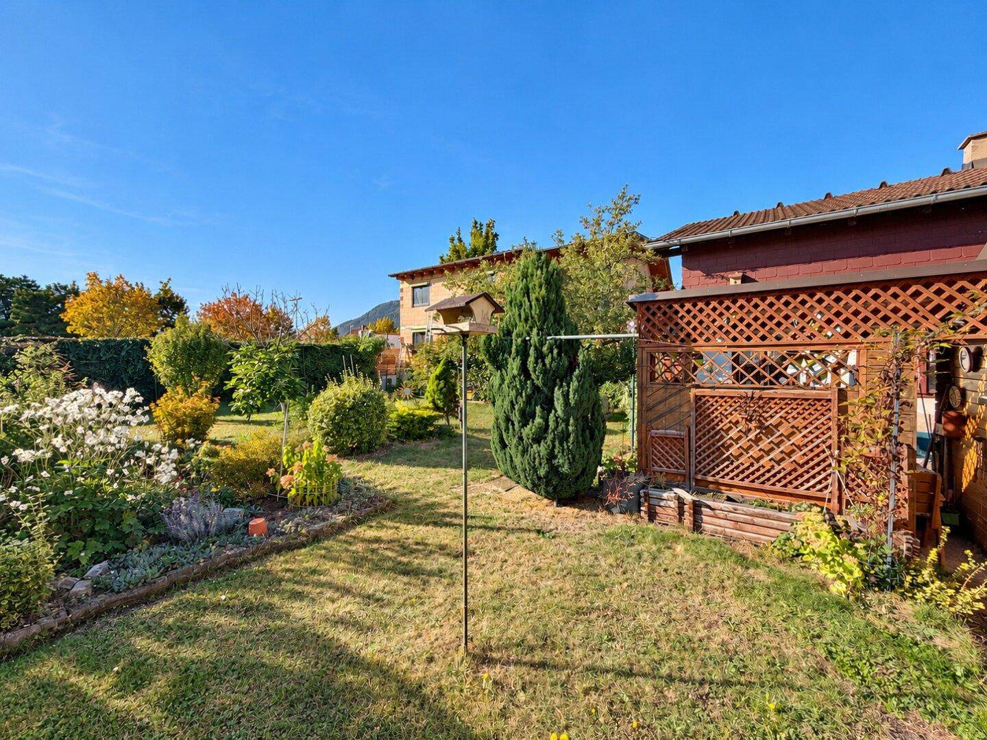 Weitläufiger Gartenbereich mit Rasen, Blumenbeeten und einem Holzschuppen im Hintergrund.