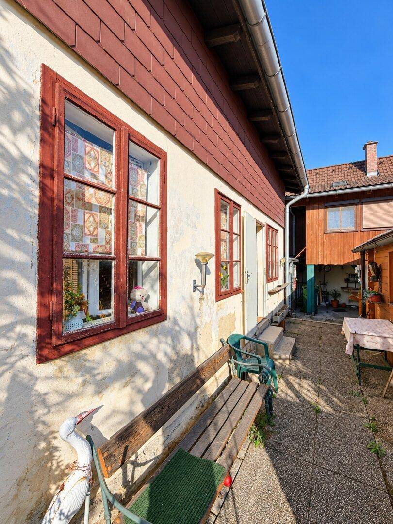 Seitenansicht eines traditionellen Hauses mit roten Fensterrahmen und einer Holzbank im Vorgarten.