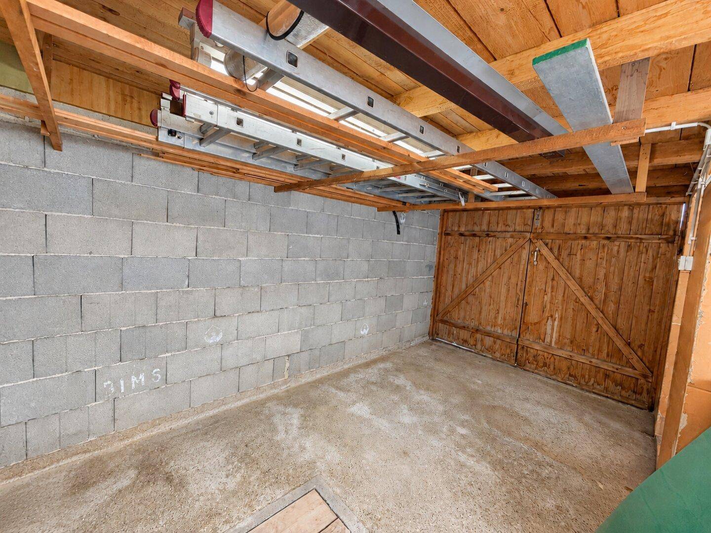 Innenansicht einer Garage mit Betonwänden, Holzdecke und Stauraum für Leitern.