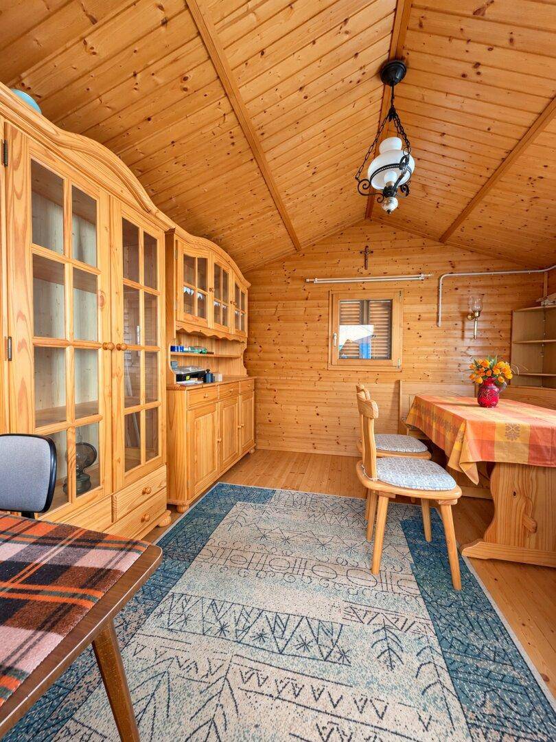 Rustikaler Innenraum einer Holzhütte mit sichtbaren Holzwänden, Dachschrägen und traditionellen Möbeln.