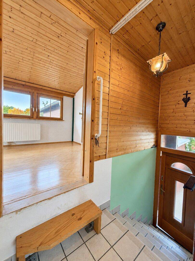 Treppenaufgang mit Holzdecke und -wänden, gefliestem Boden und Blick auf ein Fenster.