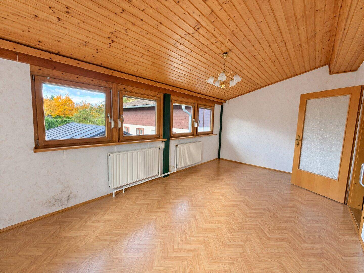 Helles Zimmer mit Holzdecke, Laminatboden und Blick auf die Umgebung durch die Fenster.