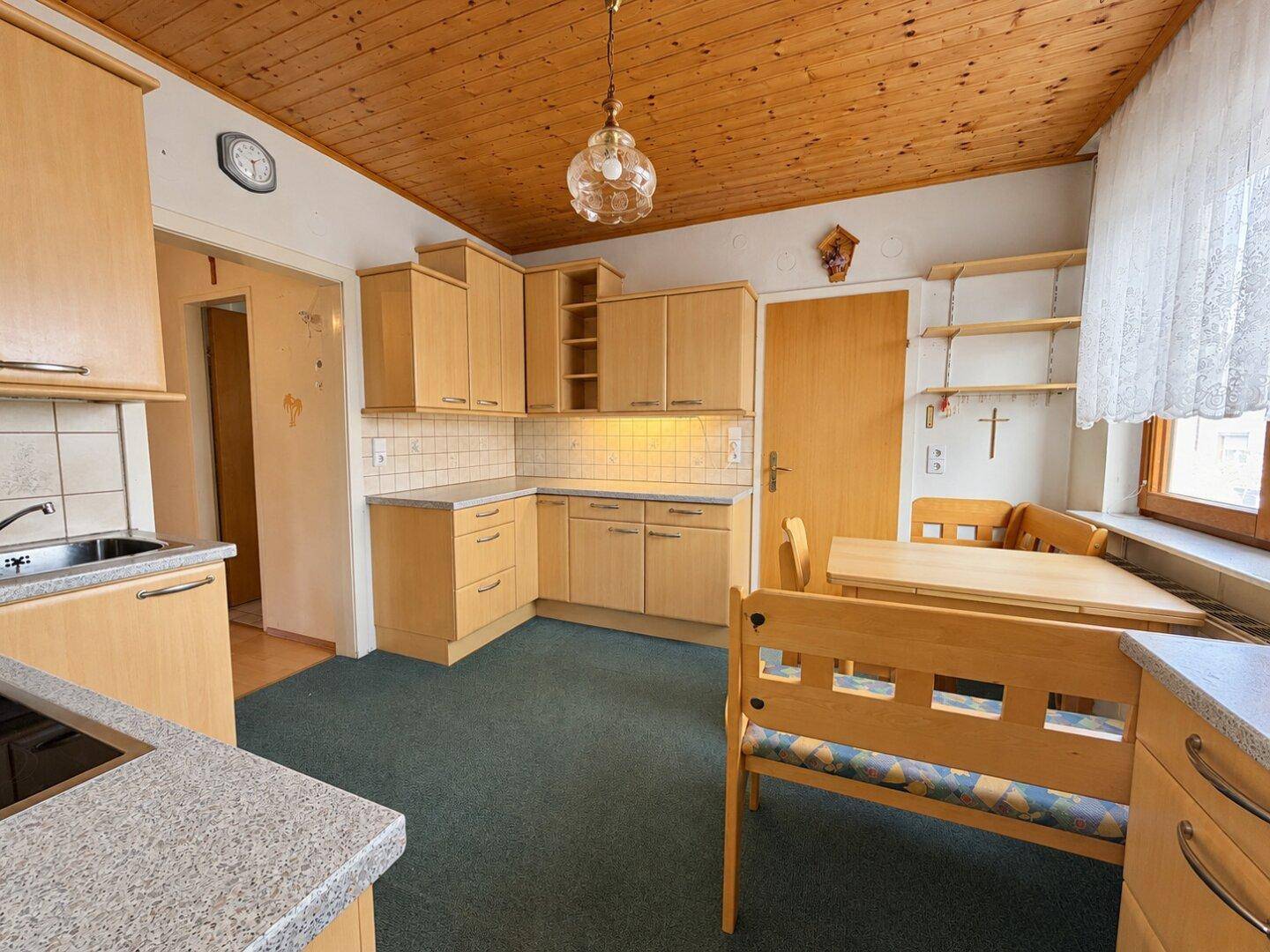 Helle Küche mit Holzdecke, Einbauküche und einem Esstisch am Fenster.
