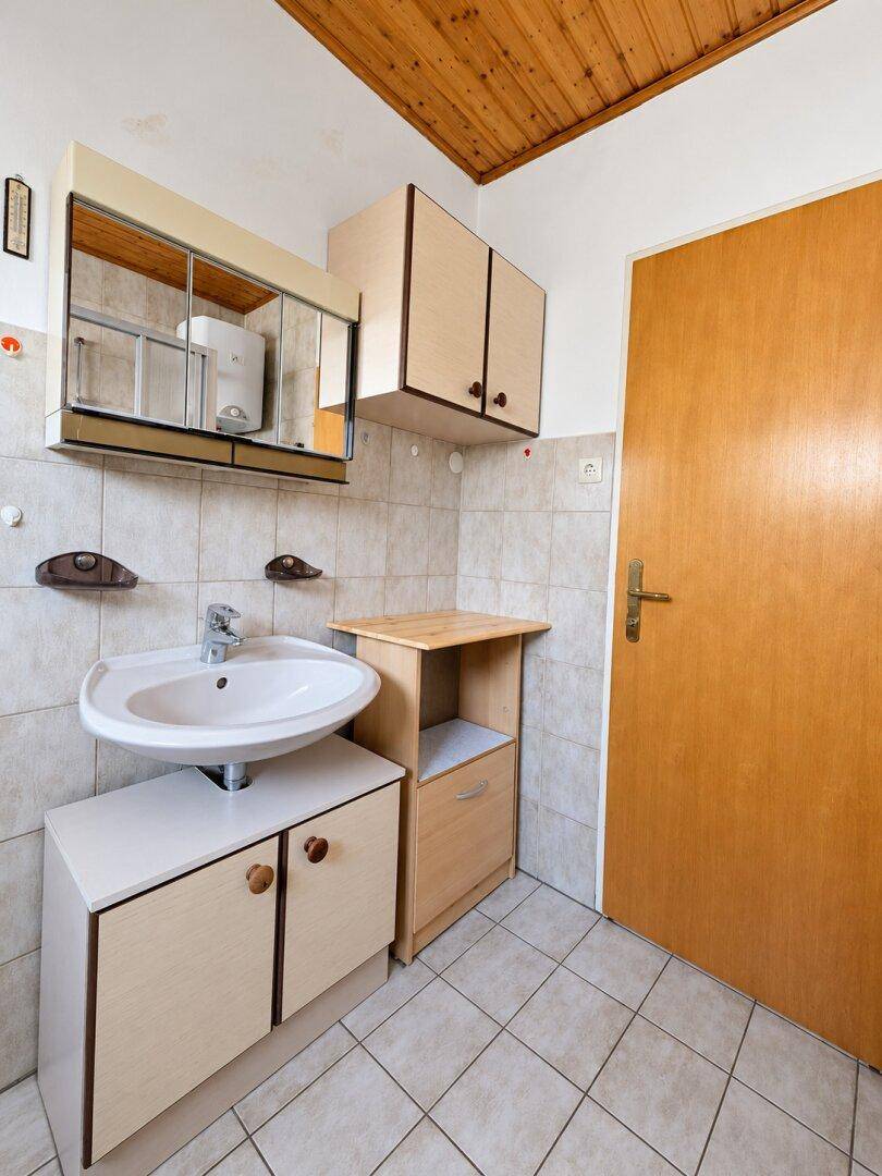 Kleines Badezimmer mit Waschbecken, Spiegelschrank und gefliesten Wänden und Boden.