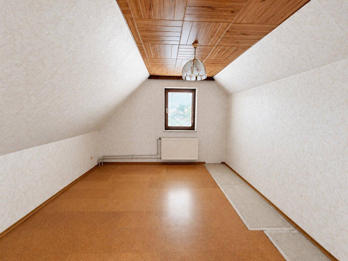 Helles Dachgeschosszimmer mit Korkboden, schrägen Wänden und einem Fenster.