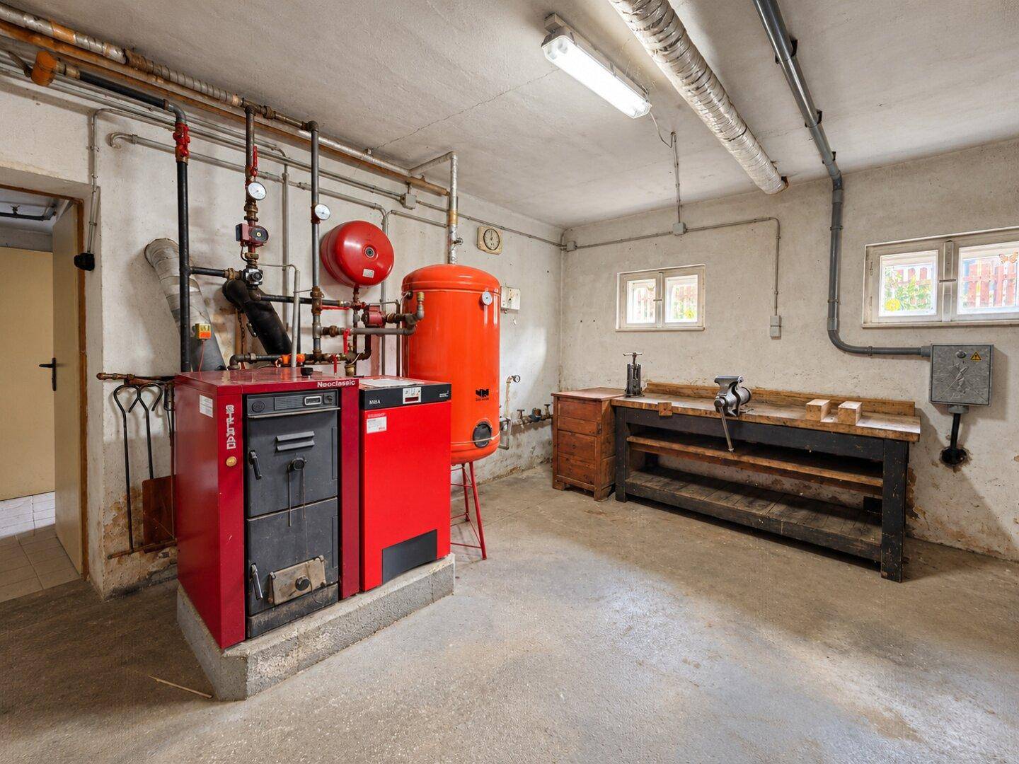 Kellerraum mit Heizungsanlage, Warmwasserspeicher und einer Werkbank mit Schraubstock.