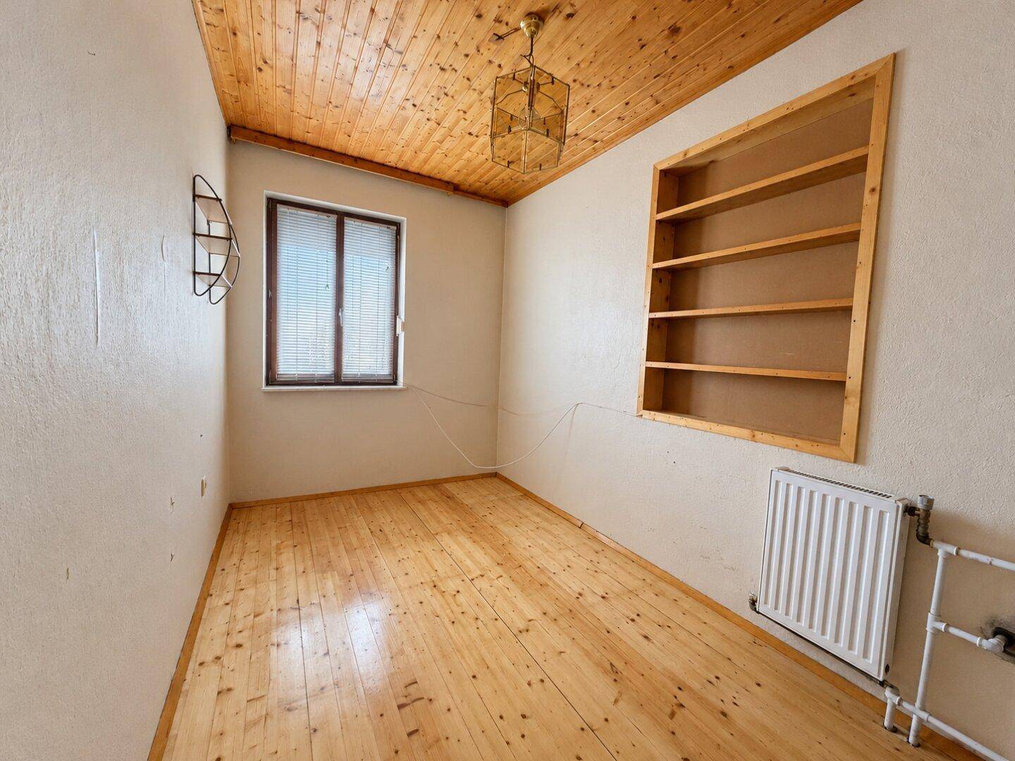 Kleines Zimmer mit Holzdielenboden, Holzdecke und einem eingebauten Regal.