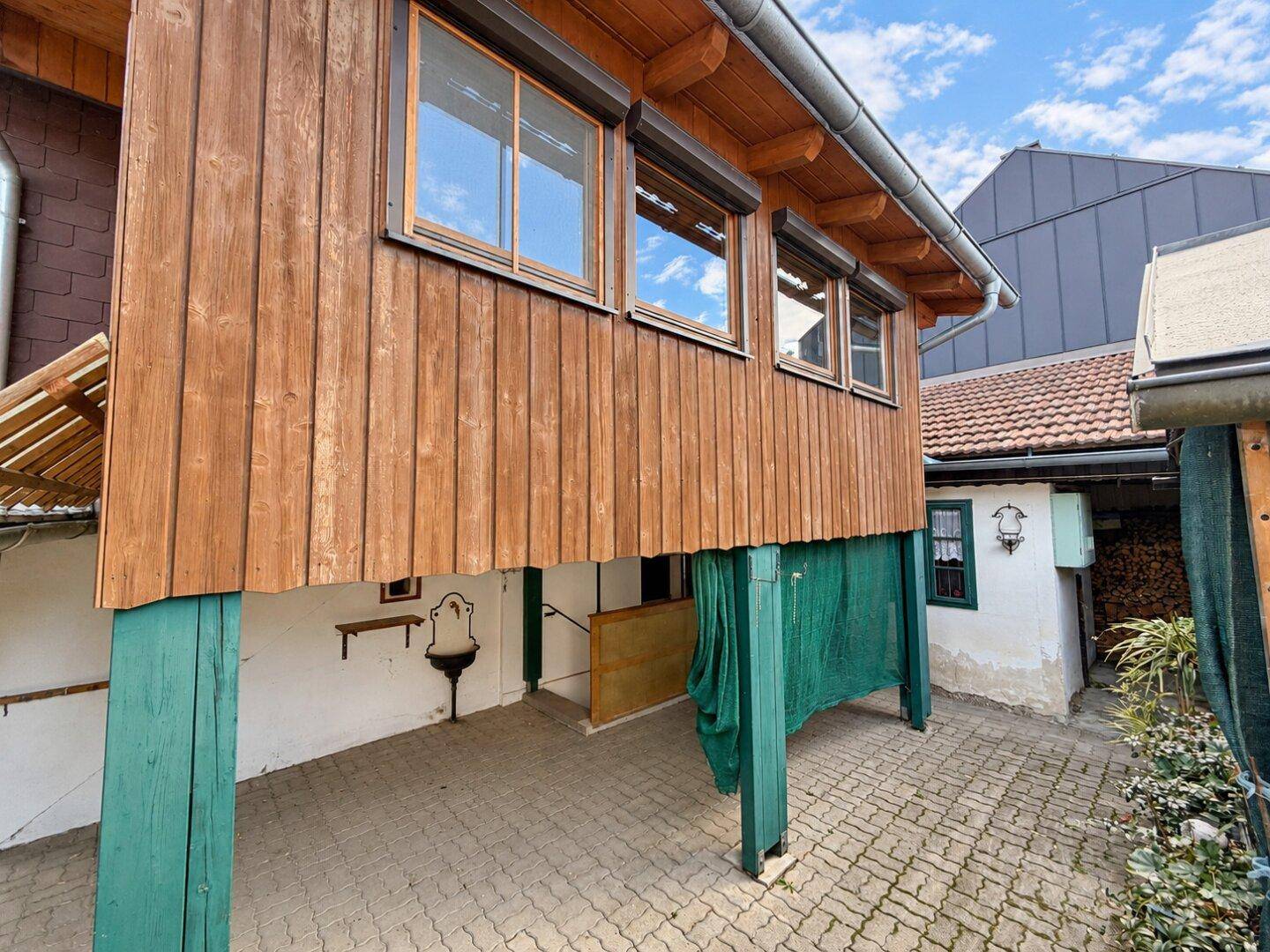 Seitenansicht des Hauses mit Holzverkleidung, überdachtem Bereich und gepflastertem Hof.