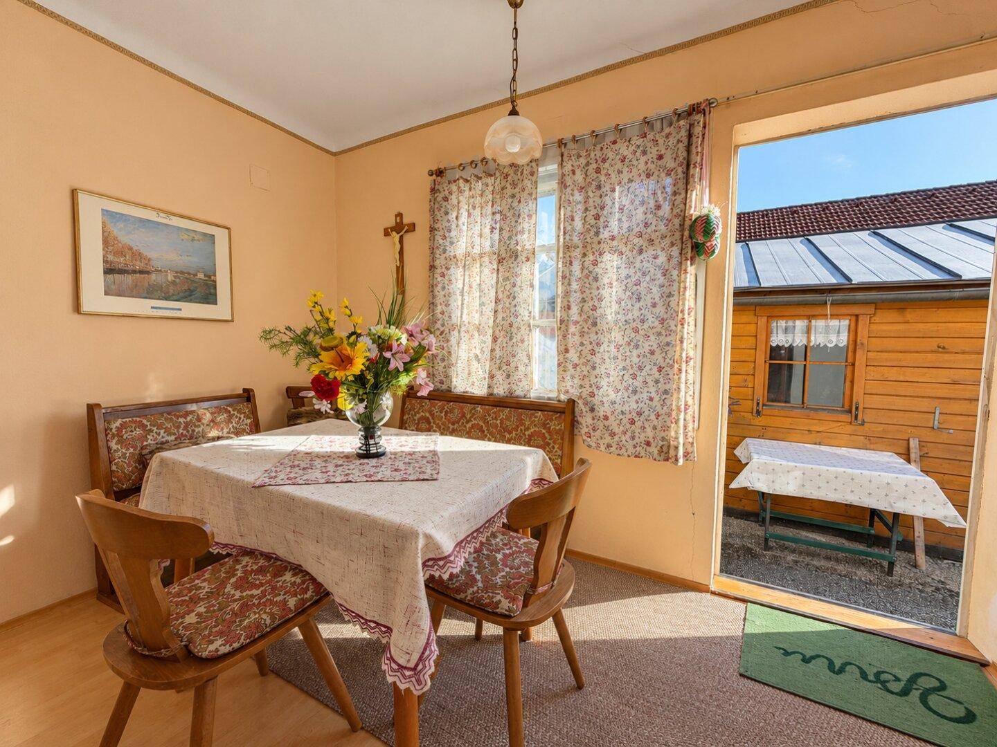 Gemütlicher Essbereich mit traditionellen Holzmöbeln, floralen Vorhängen und Blick nach draußen.
