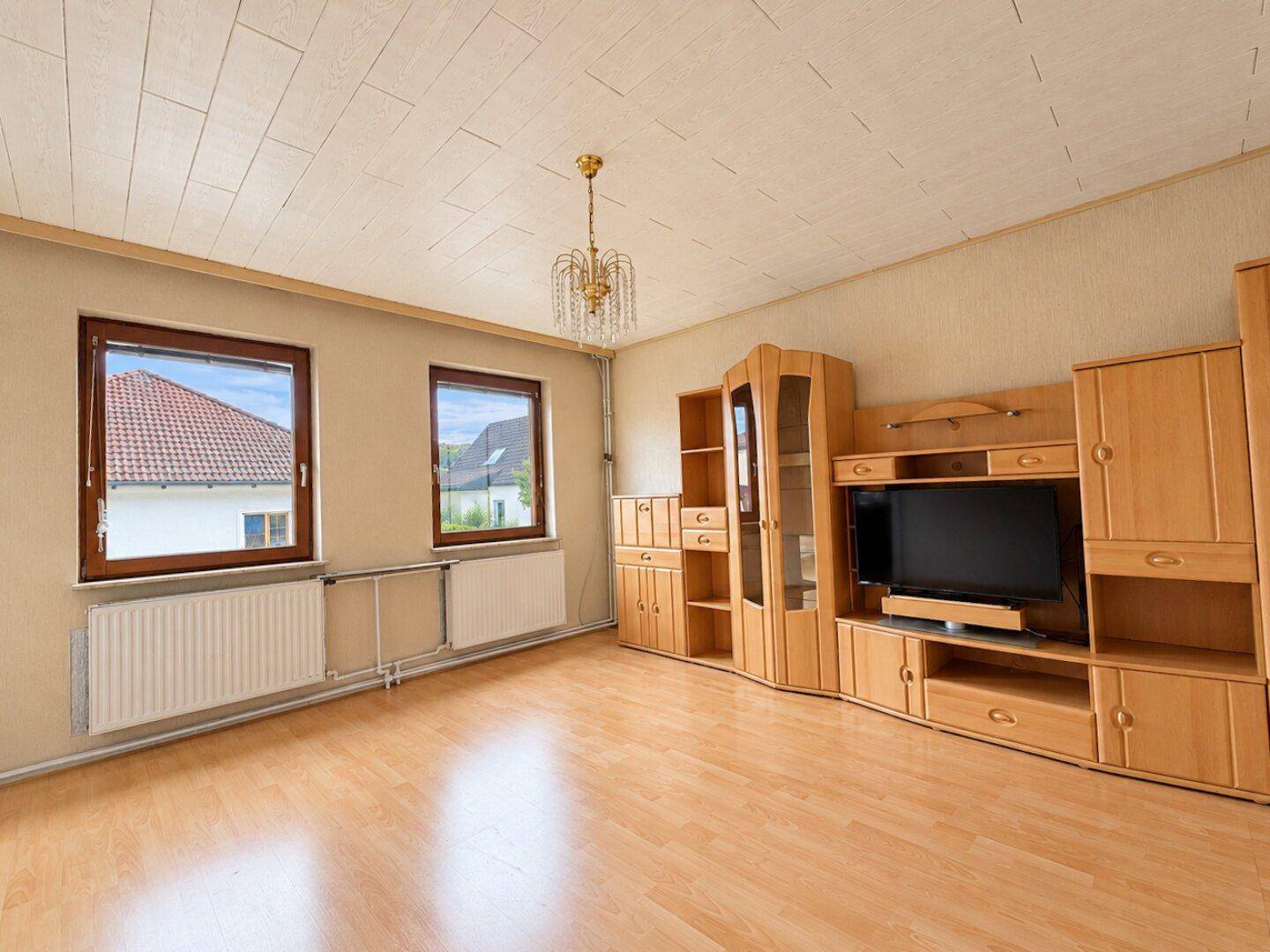 Helles Wohnzimmer mit Laminatboden, großen Fenstern und traditionellen Holzmöbeln.