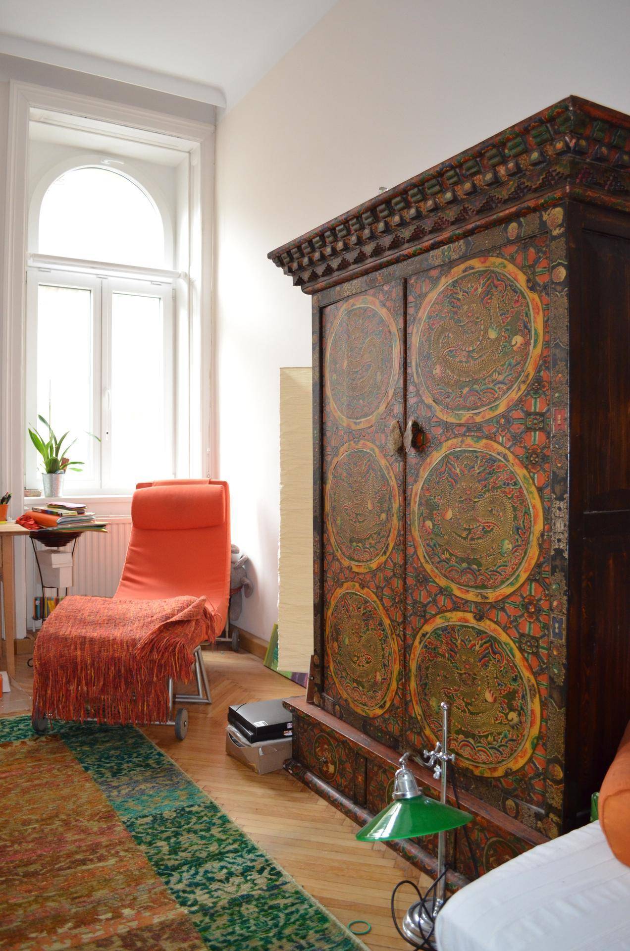 Heller Raum mit einem großen, kunstvoll verzierten Holzschrank und einem hohen Bogenfenster, das den Raum erhellt.