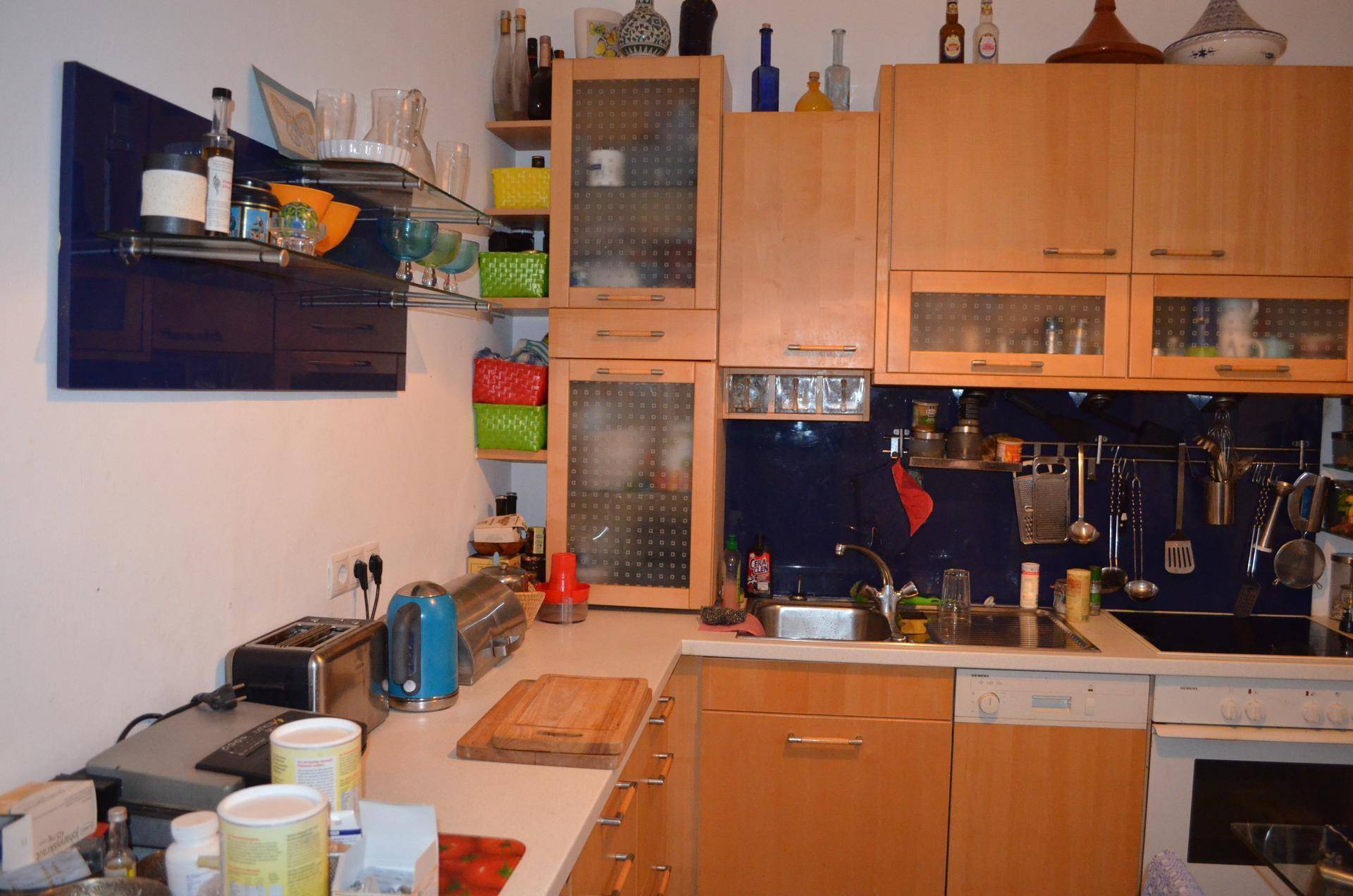 Funktionale Küche mit Holzschränken, blauer Rückwand und integrierten Geräten.