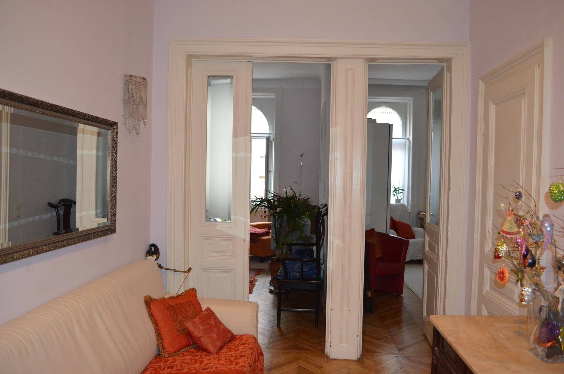 Heller Wohnbereich mit Sofa, Spiegel und Durchgang zu weiteren Zimmern mit hohen Decken.